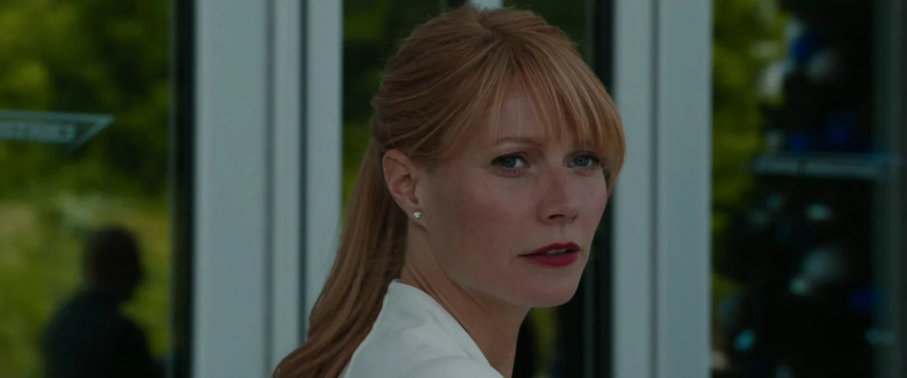 Iron Man 3 (2013) movie still: closeup — A woman stands in front of glass doors with a view of greenery outside. She turns her head to look toward…