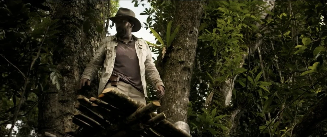 Primal (1994) movie still: medium — A man stands on a weathered wooden structure amidst a dense tropical rainforest. He looks down while dressed in…