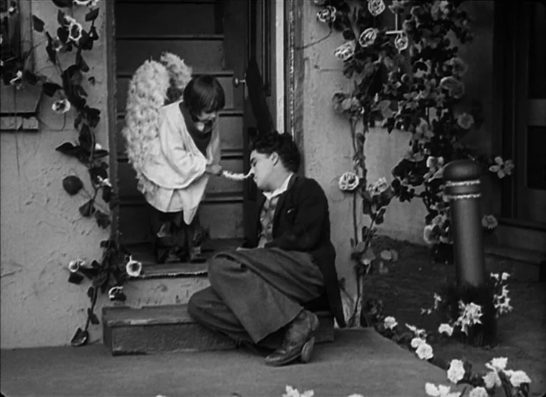 The Kid (1921) movie still: medium — A house entrance with stone steps flanked by decorative vines and roses. A young child wearing angel wings…