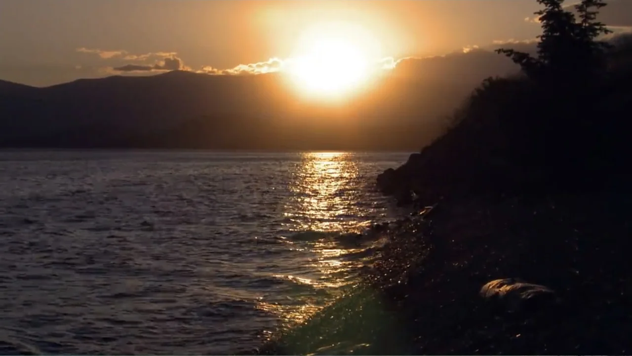 Idaho: The Movie (2012) movie still: establishing — A vast lake stretches toward distant mountains under a bright golden sunset. Light reflects…