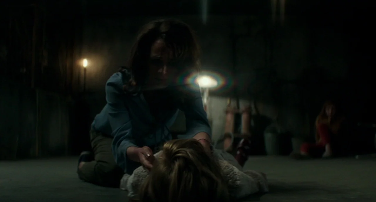 Ouija: Origin of Evil (2016) movie still: medium — A dark, unfinished room features exposed concrete walls and dimly lit corners. A woman kneels…