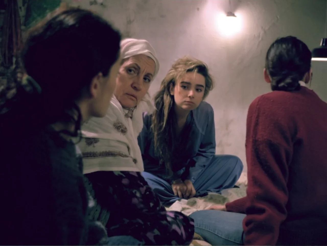 Don't Let Them Shoot the Kite (1989) movie still: medium — A dimly lit room with bare white walls and a low ceiling. Four women sit in a circle on…