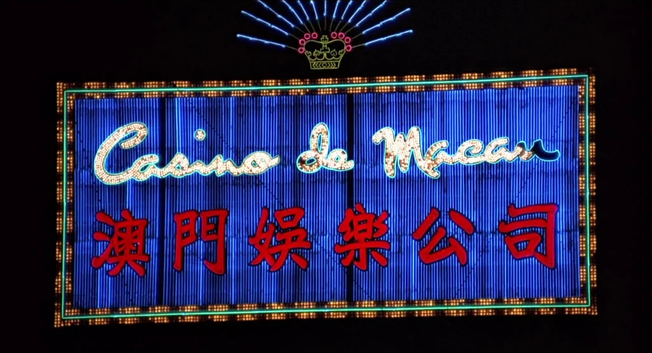 The Man With the Golden Gun (1974) movie still: establishing — A large rectangular neon sign glows brightly against a completely dark night sky. The…
