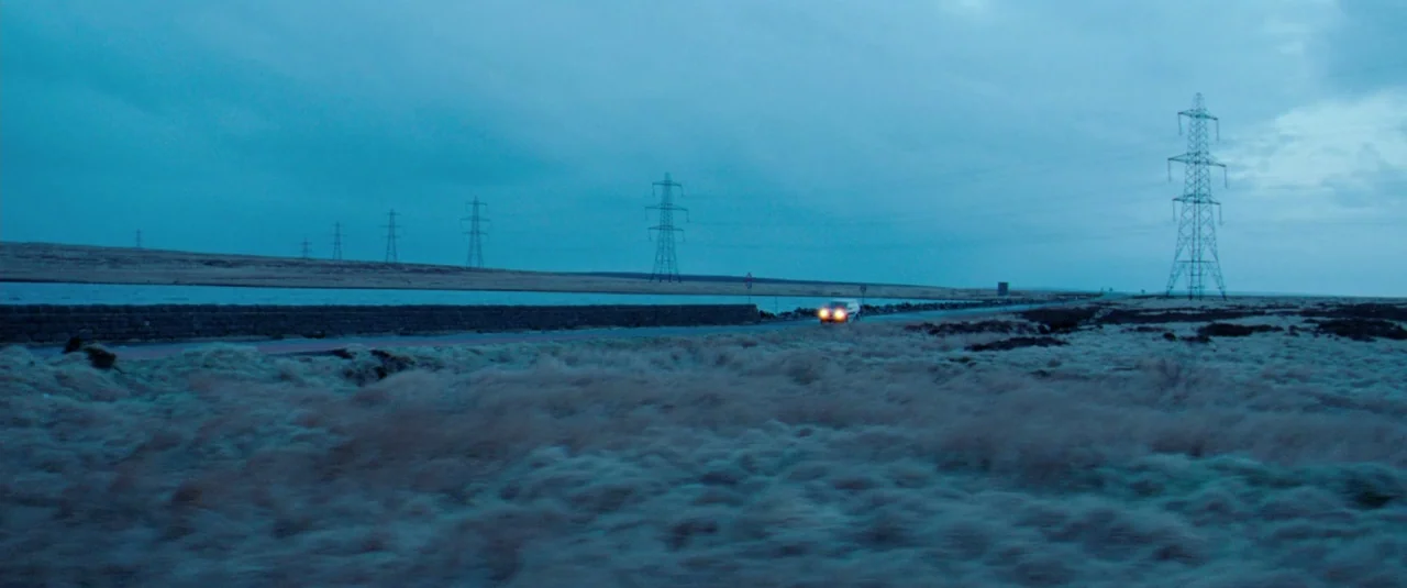 Catch Me Daddy (2014) movie still: wide — A desolate, open moorland landscape stretches under a overcast twilight sky. Electricity pylons stand in a…