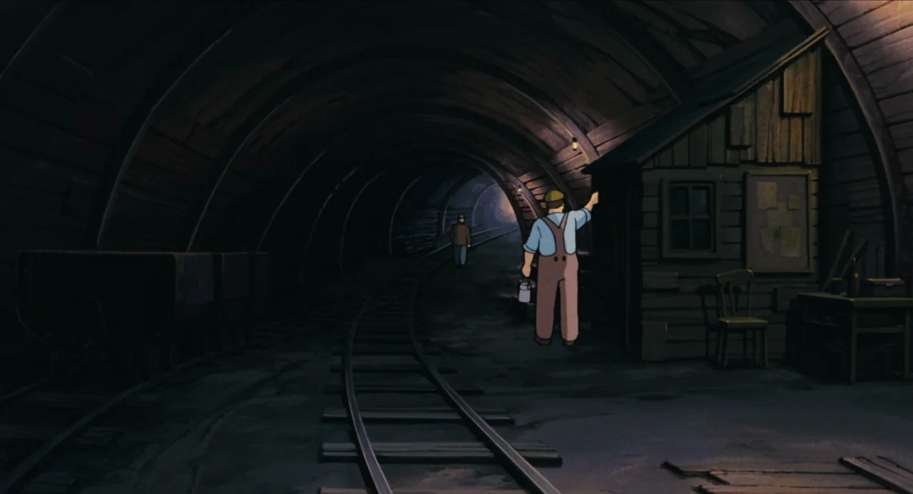 Castle in the Sky (1986) movie still: wide — A dark subterranean tunnel features curved timber supports and narrow-gauge train tracks. A man stands…