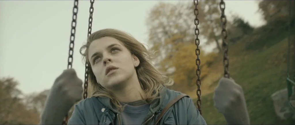 Lasting (Nieulotne) (2013) movie still: closeup — A woman sits on a playground swing set surrounded by autumnal trees. The subject looks upward…