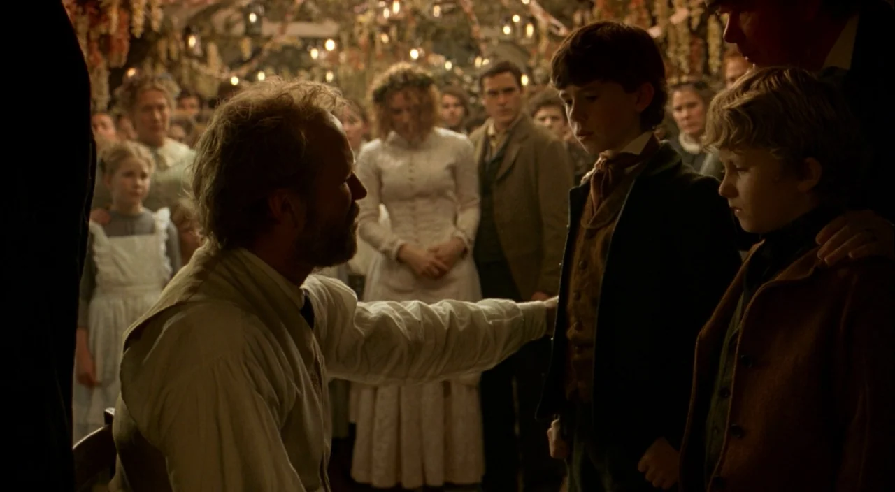 The Village (2004) movie still: medium — A dimly lit interior with a low-ceilinged structure decorated with hanging dried flora. A man sits facing…