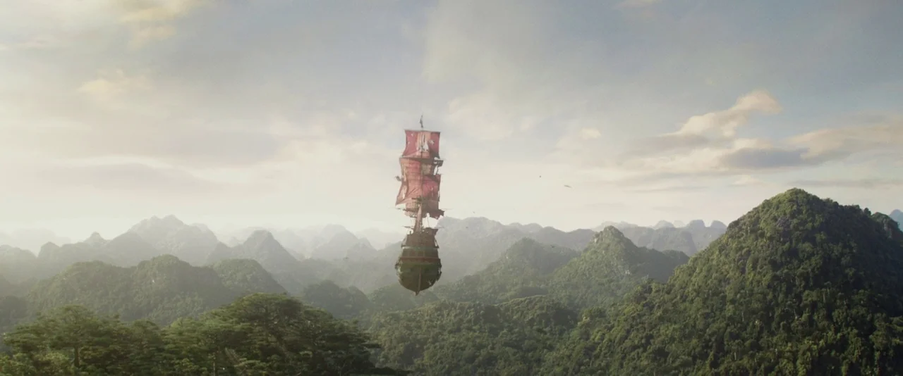 Pan (2015) movie still: establishing — A massive three-masted wooden sailing ship floats through the air over a vast mountain landscape. Green peaks…