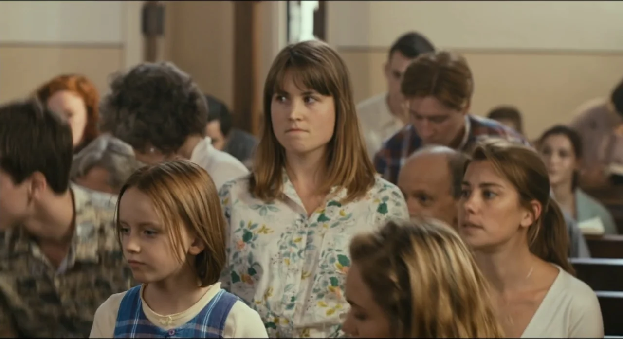 Ride Like a Girl (2019) movie still: medium — A crowded interior of a wood-paneled building with rows of wooden pews. A group of people sit or stand…