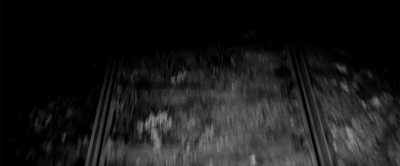 Europa (1991) movie still: establishing — A low-angle view shows two parallel metal rails receding into the dark night. Rough texture and low…