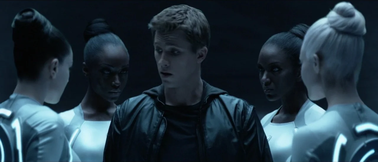 TRON: Legacy (2010) movie still: medium — A dark, indistinct space surrounds a group of five individuals in futuristic attire. A young man is…