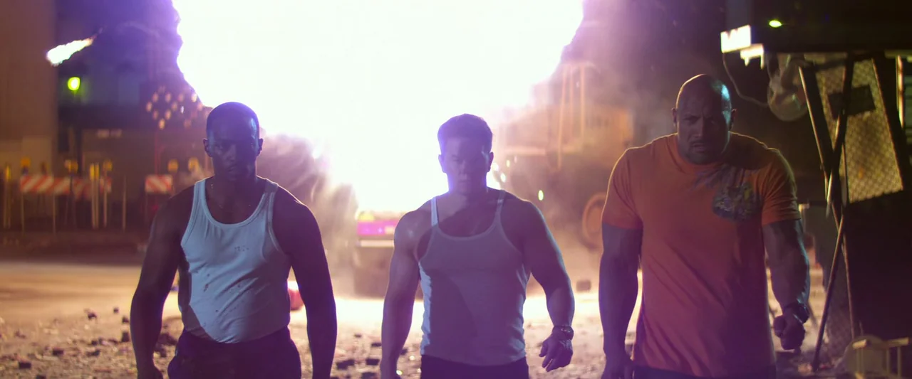 Pain & Gain (2013) movie still: fullbody — An outdoor industrial site at night is filled with debris and smoke. Three men in tank tops walk forward…