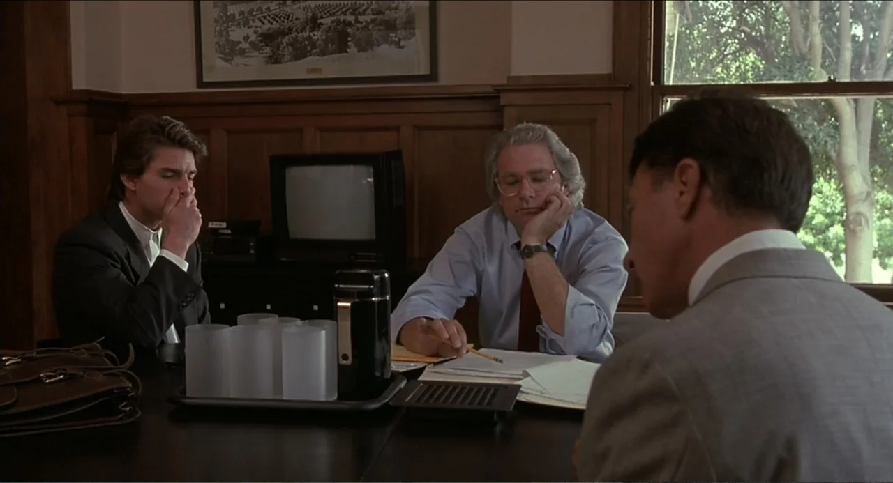 Rain Man (1988) movie still: medium — An office features wood-paneled walls, a dark conference table, and a large window. Three men in professional…