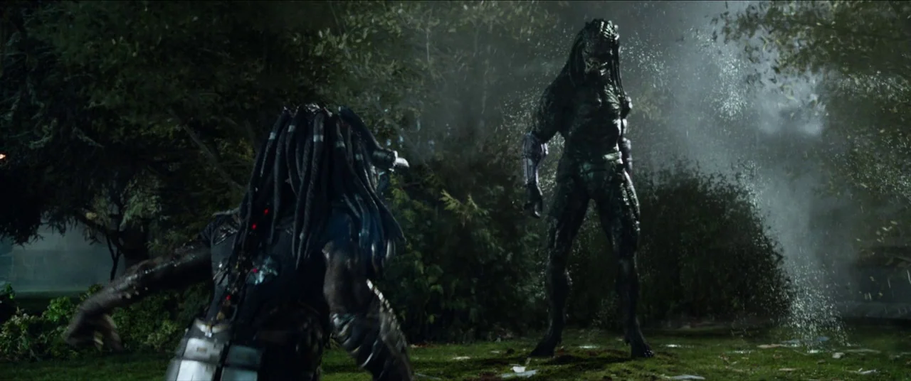 The Predator (2018) movie still: fullbody — A dark residential lawn at night with trees and shrubs framing the central figures. Two armored…