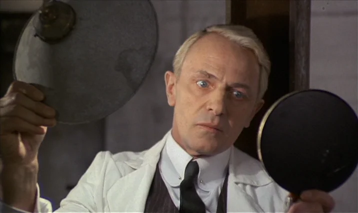 The Serpent’s Egg (1977) movie still: closeup — A clinical examination room with plain walls and medical equipment background elements. A…