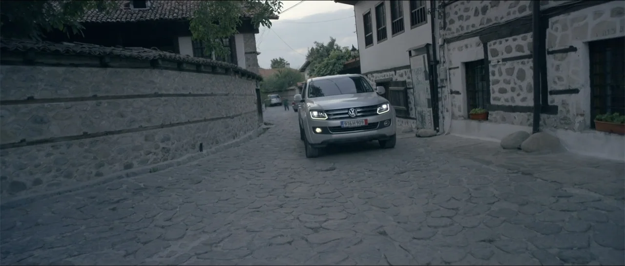 All She Wrote (2018) movie still: medium — A narrow cobblestone street is flanked by traditional white stone buildings with dark wooden accents. A…