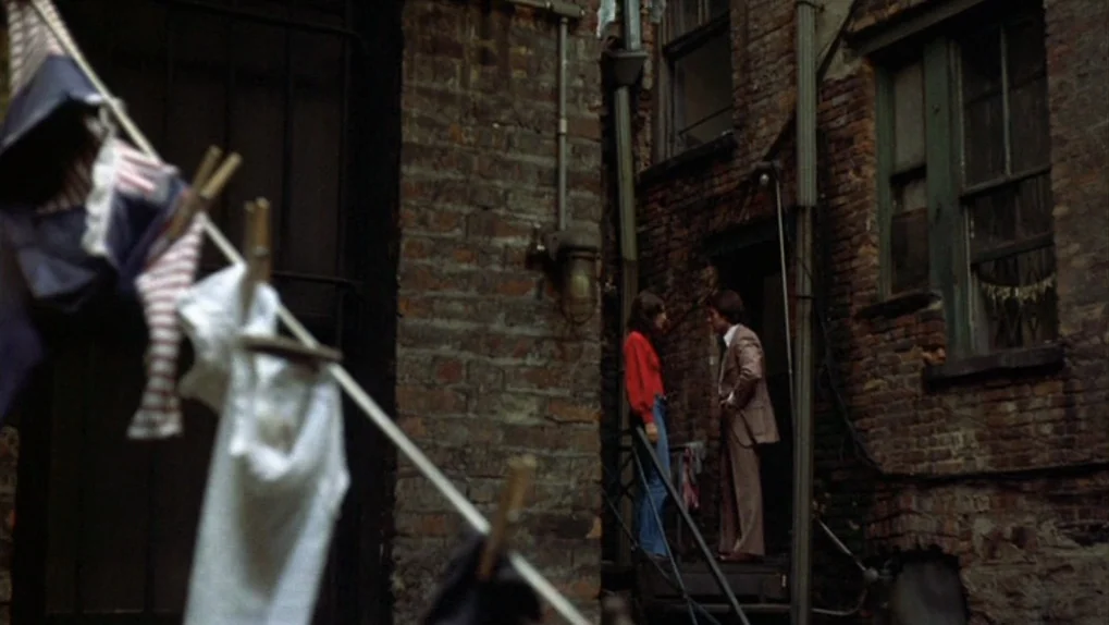 Mean Streets (1973) movie still: wide — A narrow urban space with weathered dark brick walls and aged metal fixtures. A man and a woman interact on…
