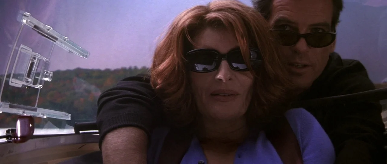 The Thomas Crown Affair (1999) movie still: medium — A man and woman ride in a motorboat with a transparent windshield. The background displays a…