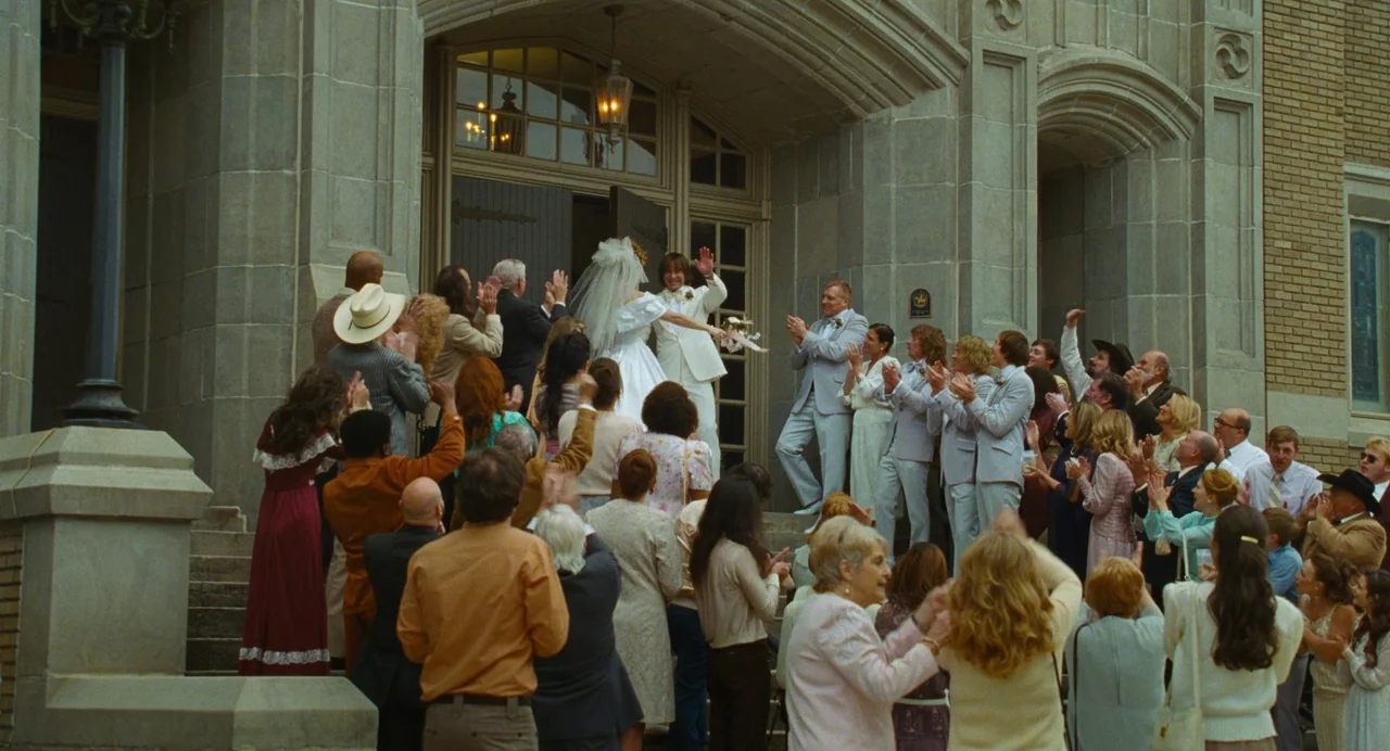 The Iron Claw (2023) movie still: wide — A stone-clad building with arched doorways hosts a large group of wedding guests. The newly married couple…