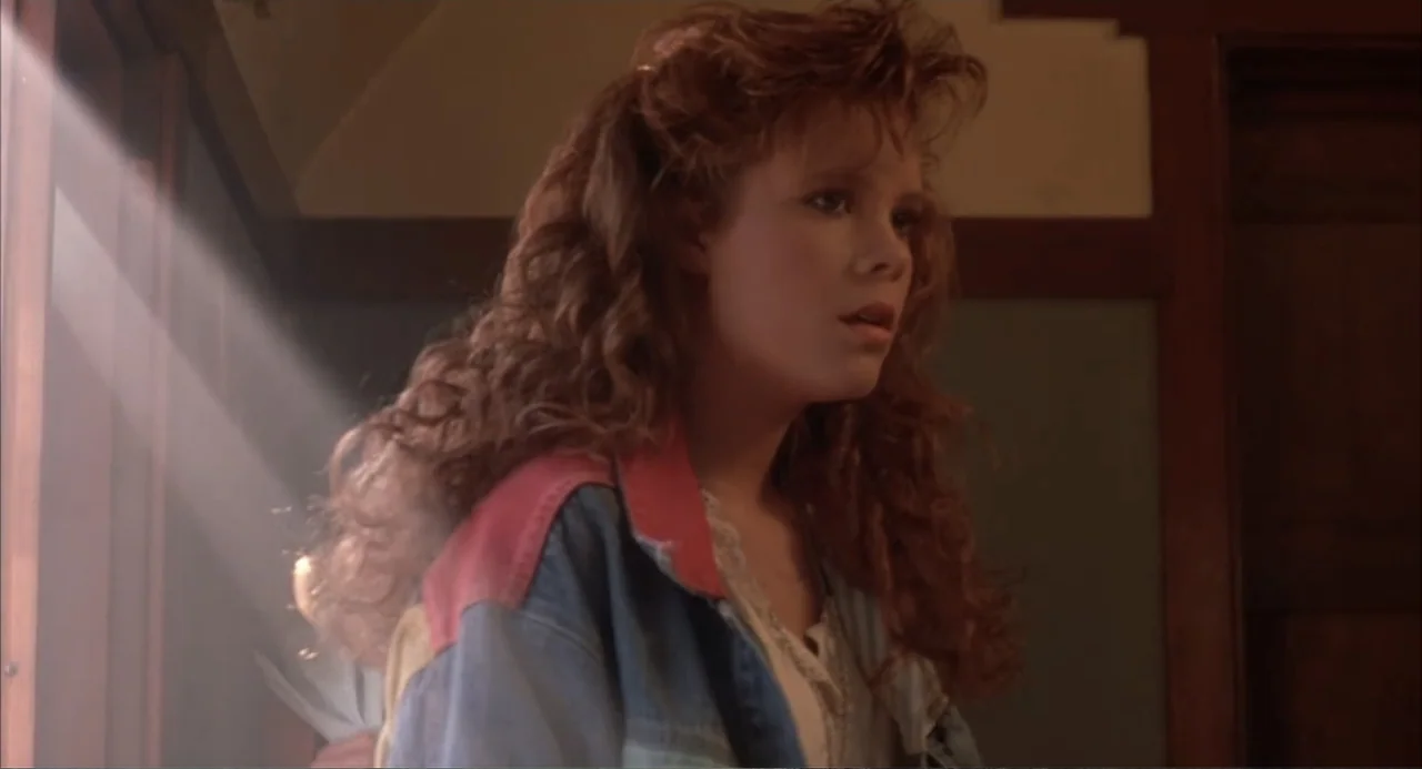 Teen Witch (1989) movie still: medium — An interior space features muted wall colors and wood trim illuminated by side-lighting. A young woman with…