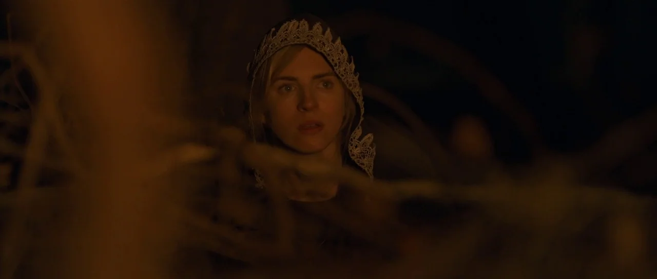 The East (2013) movie still: closeup — A woman stands in a dark wooded area at night surrounded by dry twigs. The subject is partially obscured by…