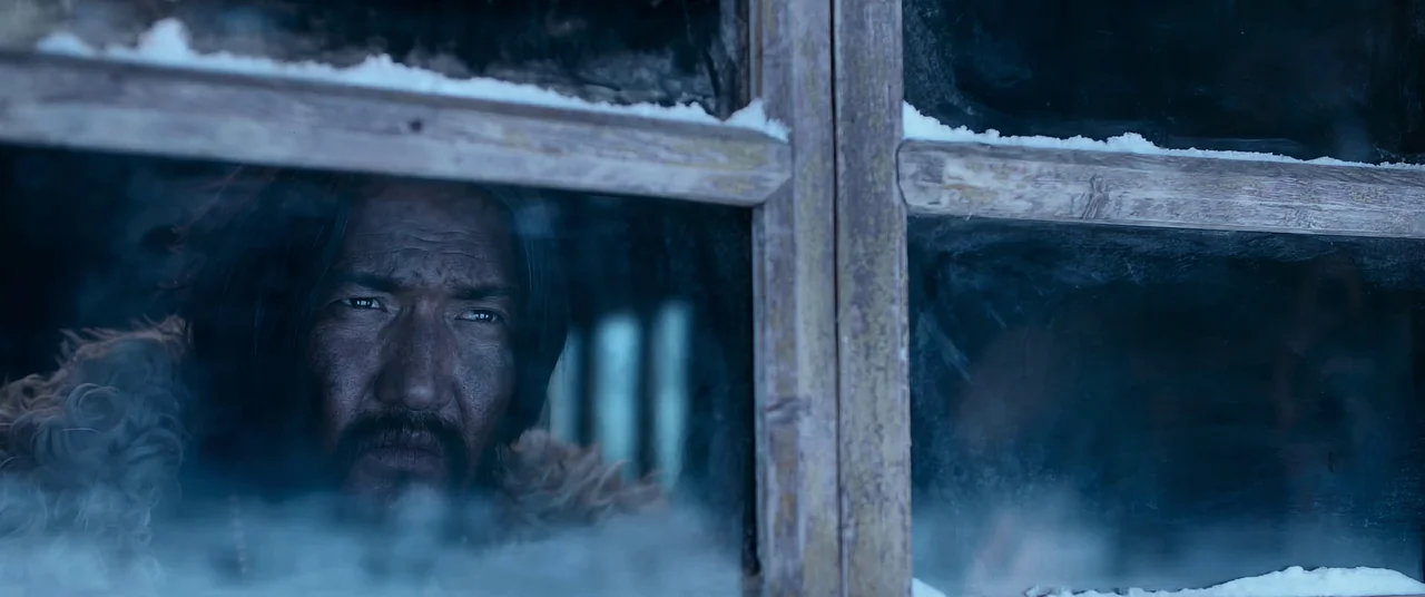 One And Four (2021) movie still: closeup — A man peers through the pane of a weathered, wooden-framed window covered in frost. Snow rests on the…