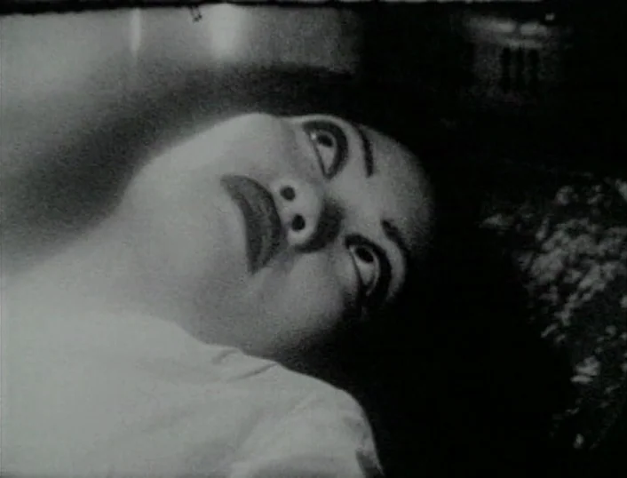 Cowards Bend The Knee (2003) movie still: closeup — A close up on a face in a dark, shadow-filled environment. The subject rests against a textured…