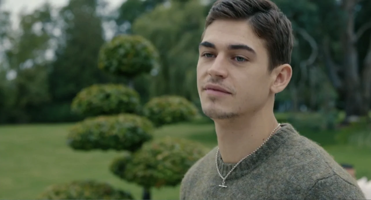 Picture This (2008) movie still: medium — A man stands outdoors in front of manicured green shrubs. He gazes to the side while standing in a park.