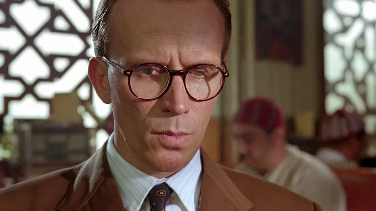 Naked Lunch (1991) movie still: closeup — A man stands inside a building with large decorative geometric lattice window grilles. He looks downwards…