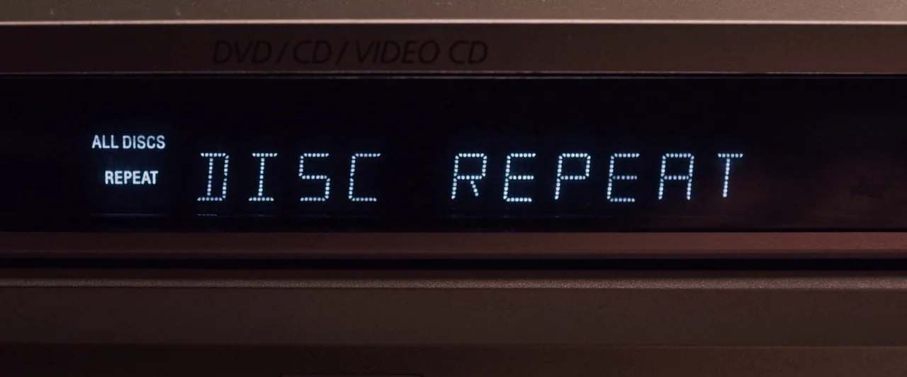 You’re Next (2013) movie still: closeup — A close-up view of a metallic media player display with glowing text. The text reads DISC REPEAT in a…
