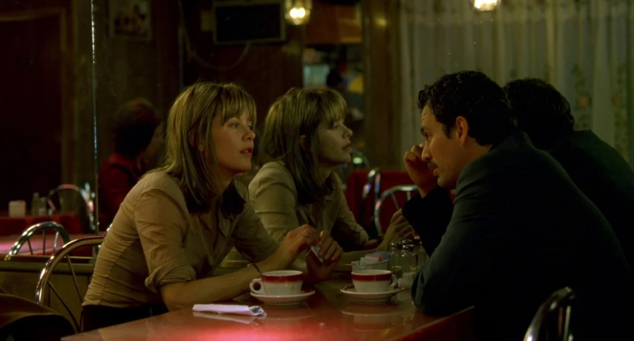 In The Cut (2003) movie still: medium — A dimly lit diner booth features wood-paneled walls and a mirrored back. A man and a woman sit facing each…
