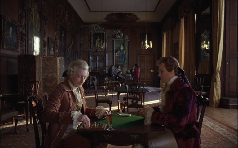 Barry Lyndon (1975) movie still: medium — A dark wood-paneled room is decorated with numerous oil paintings in elaborate gold frames. Two men sit at…