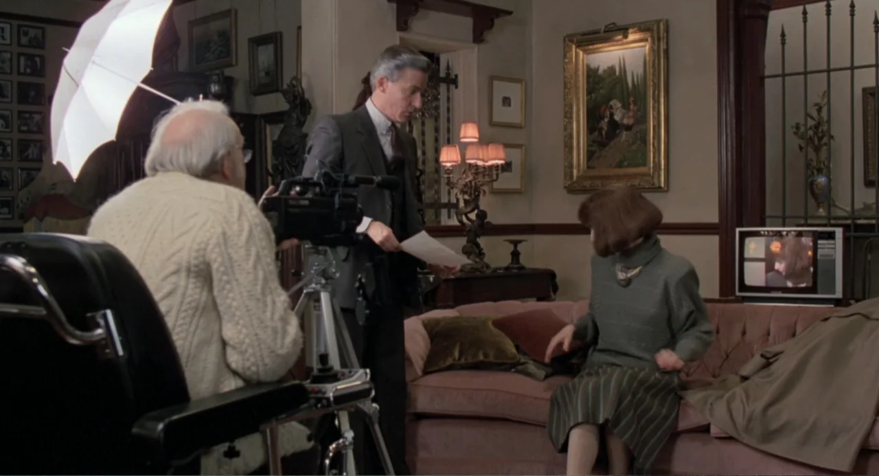 Dead of Winter (2025) movie still: medium — An interior living room features a pink sofa, traditional oil paintings, and iron grillwork. A…