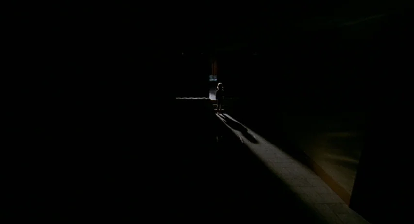 The Fifth Cord (1971) movie still: wide — A dark, empty interior corridor features a single bright rectangular doorway at the end. A small child…