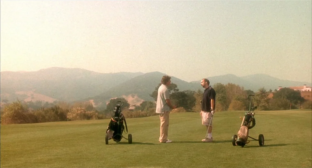 Sideways (2004) movie still: wide — A green hilly landscape on a golf course under a hazy clear sky. Two men stand in the middle of the grass…