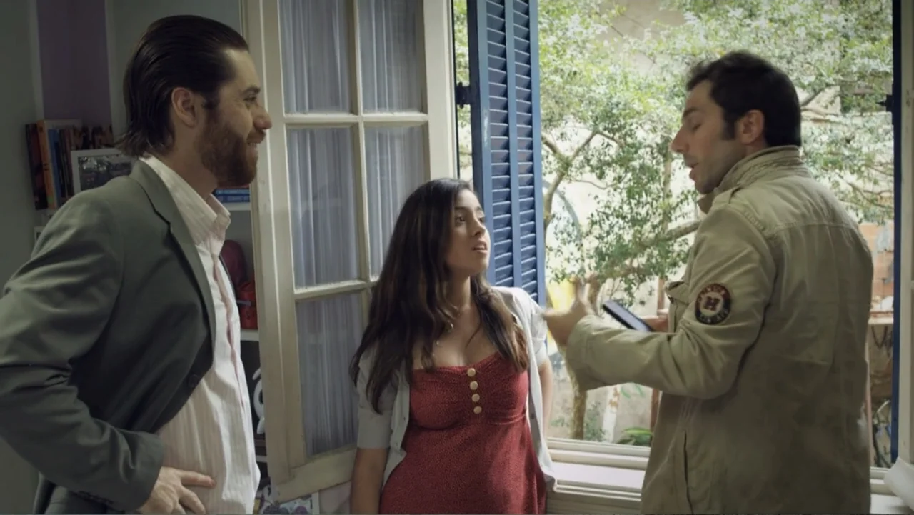 For Sale or Rent (2013) movie still: medium — An indoor space with a large window and blue shutters looking out to trees. Two men and a woman are…