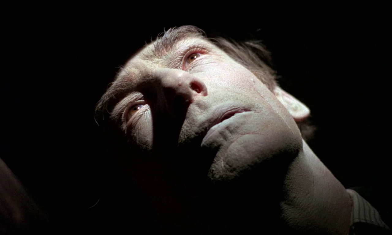 Curse of the Crimson Altar (1968) movie still: closeup — A man's head is illuminated by a sharp light against a dark background. He is looking…
