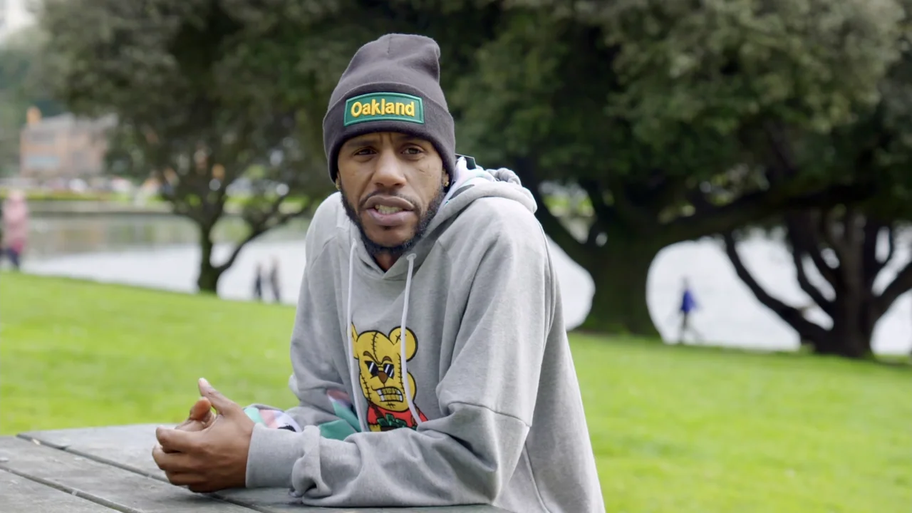 We Are the Dream: The Kids of the Oakland MLK Oratorical Fest (2020) movie still: medium — A man sits at a weathered picnic table in a green public…
