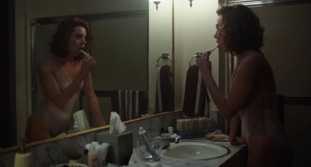 An Evening With Beverly Luff Linn (2018) movie still: medium — A dimly lit bathroom features a large wall mirror and marble-patterned vanity…