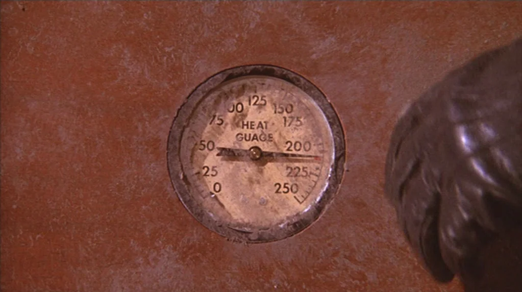 The Ballad of Cable Hogue (1970) movie still: closeup — A weathered, circular analog heat gauge is embedded in a textured, reddish-brown wall…