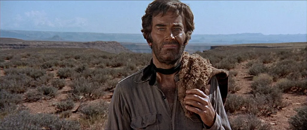 Once Upon A Time In The West (1968) movie still: medium — A vast, arid desert landscape stretches toward distant mesas under a clear sky. A man with…
