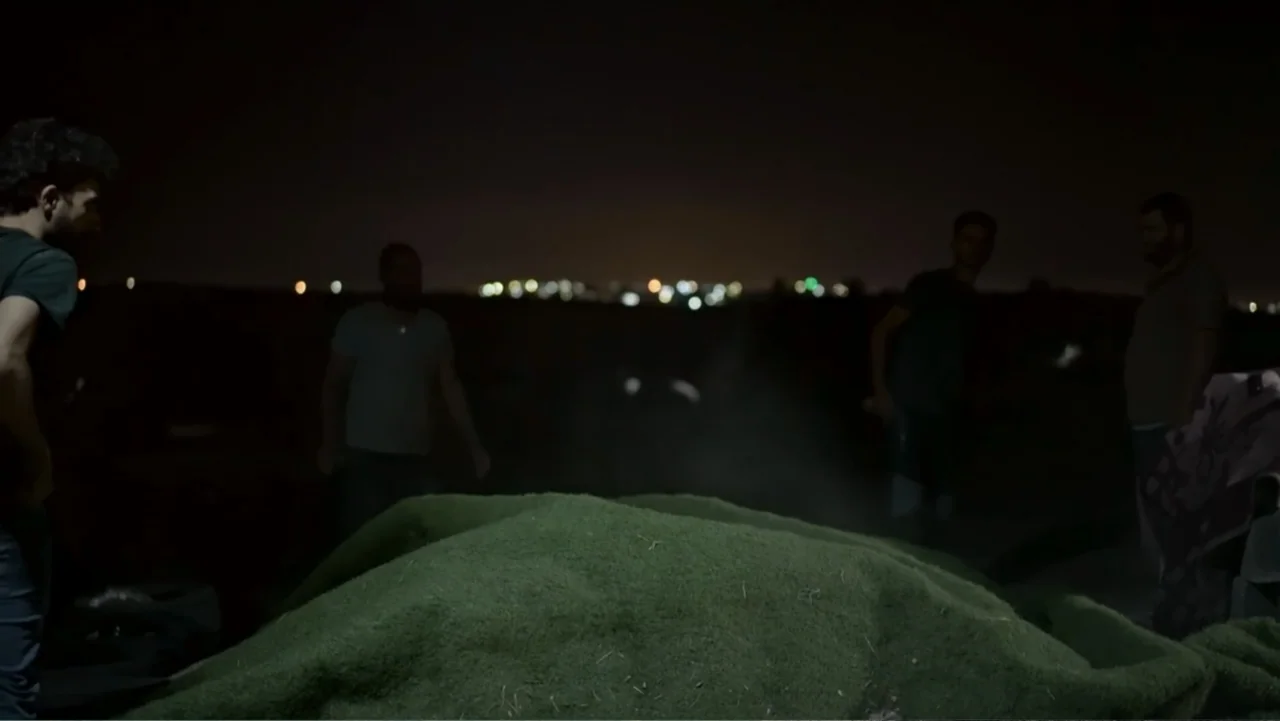 No Other Land (2024) movie still: medium — An open field at night features a pile of artificial green turf in the center. Four men stand around the…