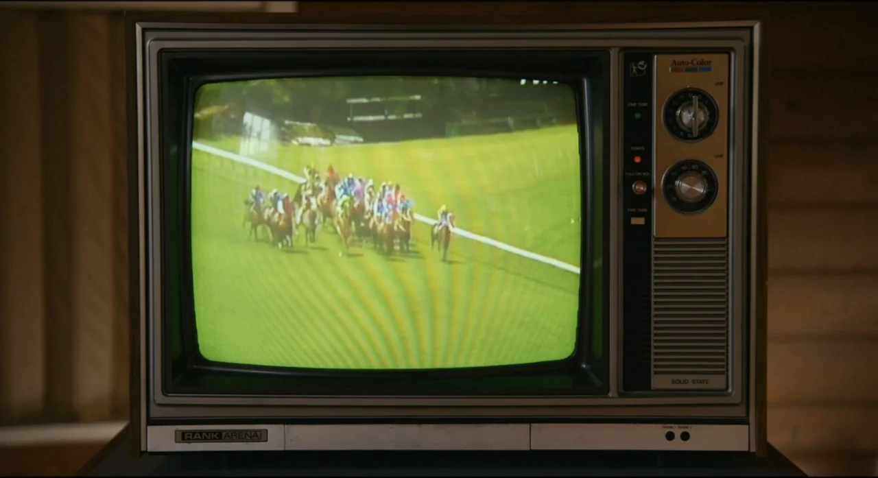 Ride Like a Girl (2019) movie still: medium — A vintage wood-paneled Rank Arena television set occupies the center of the frame. The screen displays…