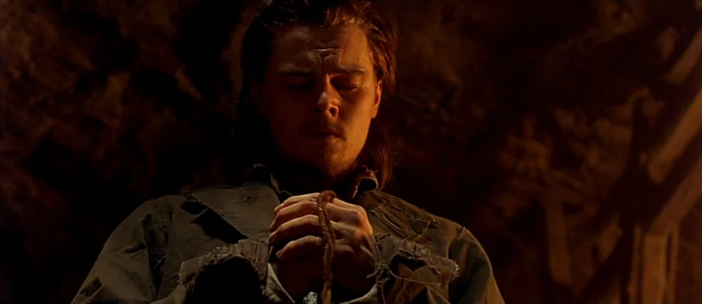Gangs of New York (2002) movie still: medium — A dimly lit cave interior with rocky walls shrouded in deep shadows. A young man with long hair…