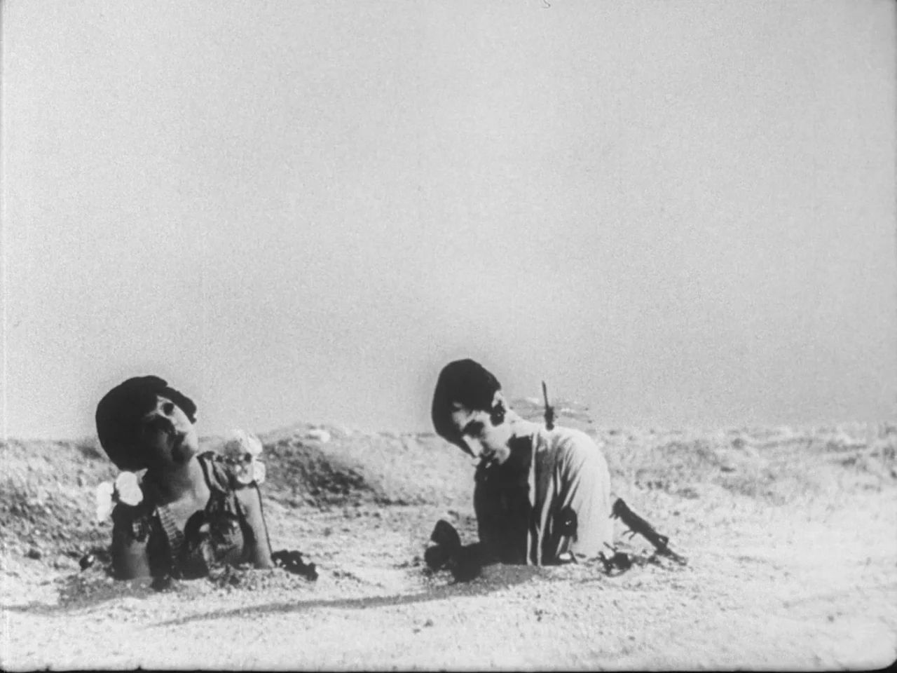 Un Chien Andalou (1929) movie still: wide — A vast, barren sandy landscape stretches across the frame under a bright sky. A woman and a man are…