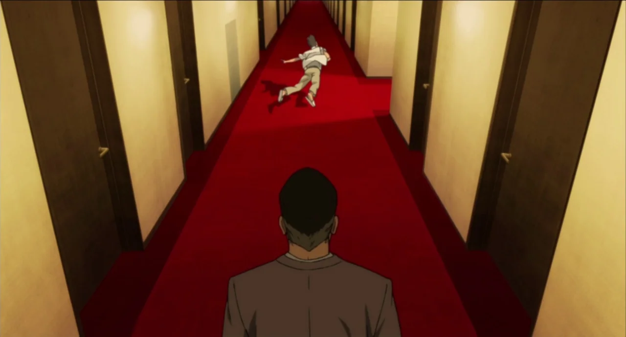 Paprika (2006) movie still: wide — A long, symmetrical indoor corridor features a deep red carpet and yellow-walled sides. A man in a suit stands in…