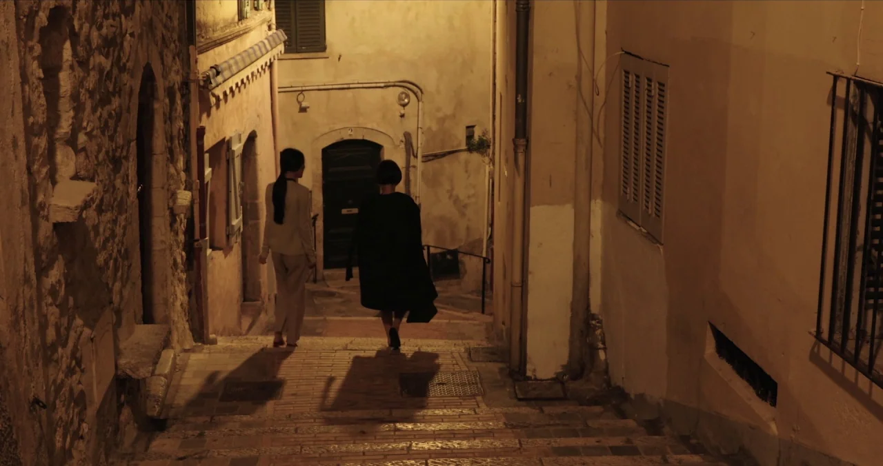 Claire’s Camera (2017) movie still: fullbody — A narrow European-style stone alleyway features weathered plaster walls and steep descending stairs.…