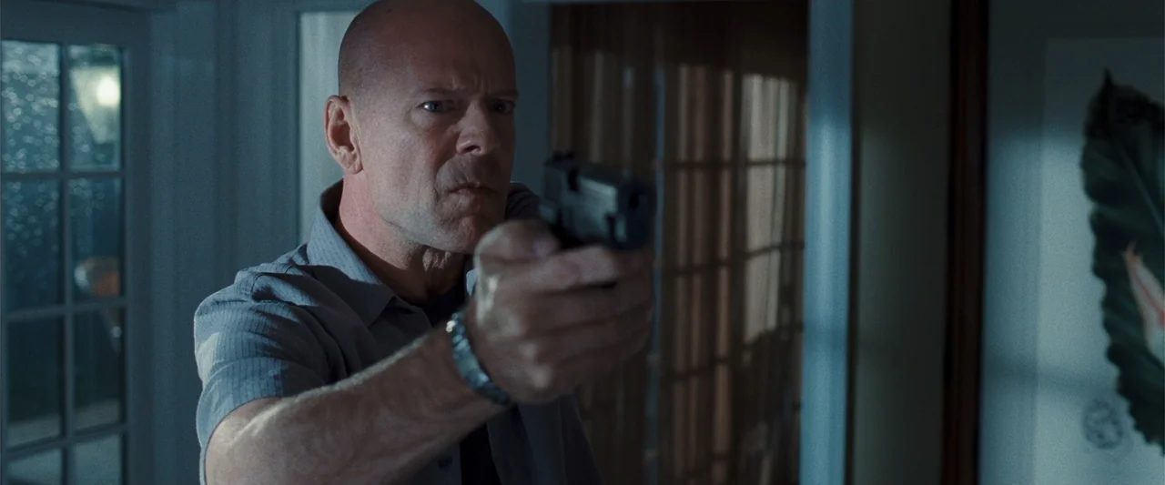 Cop Out (2010) movie still: medium — A dimly lit indoor space features a man positioned near a window with curtains. The man aims a handgun directly…