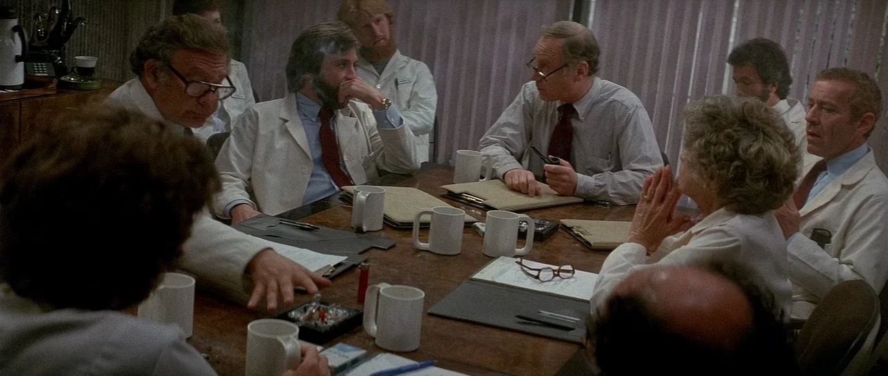 The Entity (1982) movie still: medium — A group of doctors in white coats gather around a large wooden table. They are holding a meeting with…