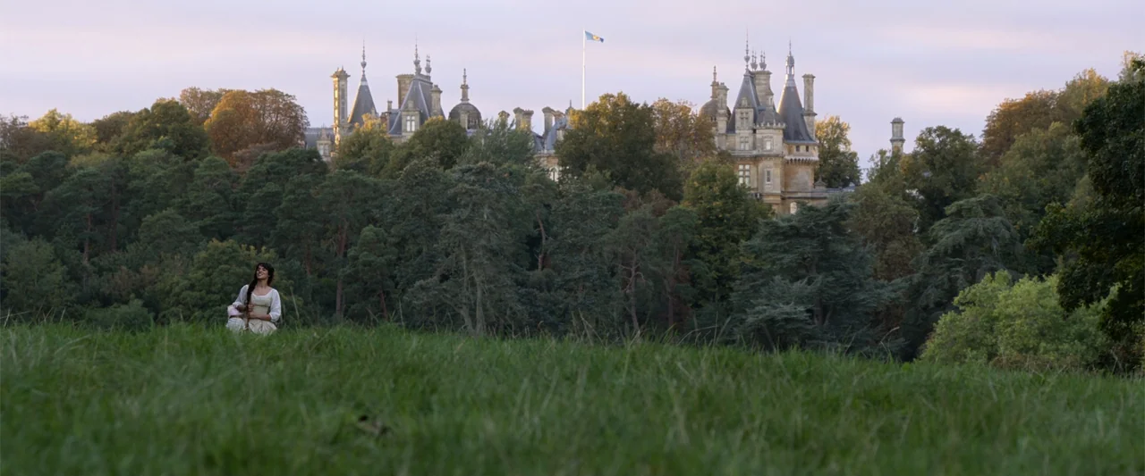 Cinderella (2015) movie still: wide — A vast estate lawn with a large stone manor visible behind dense green trees. A young woman in period clothing…
